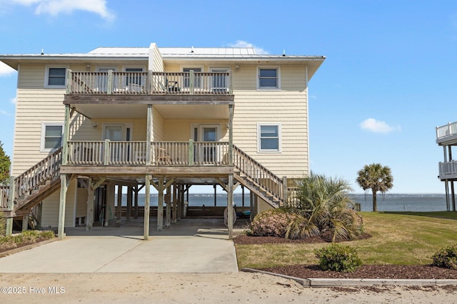 back of property with a carport, stairway, a water view, a balcony, and driveway