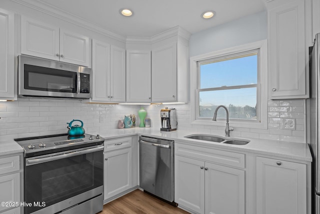 kitchen featuring appliances with stainless steel finishes, a sink, white cabinets, backsplash, and recessed lighting
