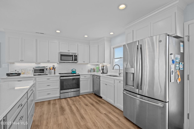 kitchen with stainless steel appliances, a sink, white cabinetry, light wood-style floors, and decorative backsplash