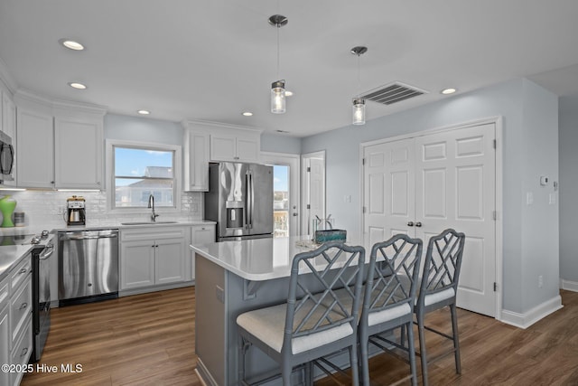 kitchen with appliances with stainless steel finishes, a sink, a breakfast bar area, white cabinetry, and recessed lighting