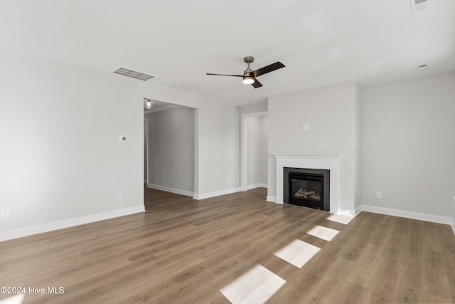 unfurnished living room featuring a ceiling fan, light wood-type flooring, a glass covered fireplace, and baseboards