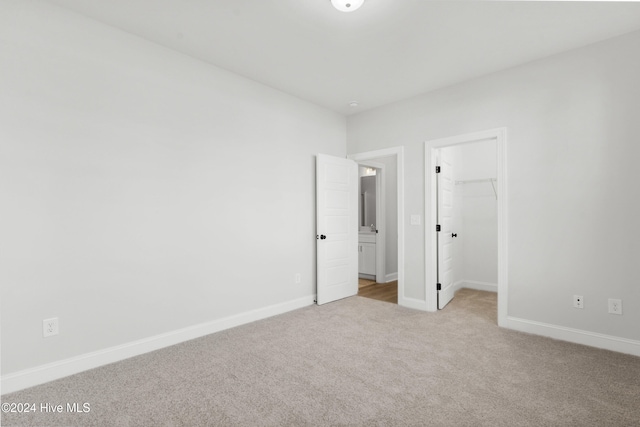 unfurnished bedroom featuring light colored carpet, a spacious closet, baseboards, and a closet