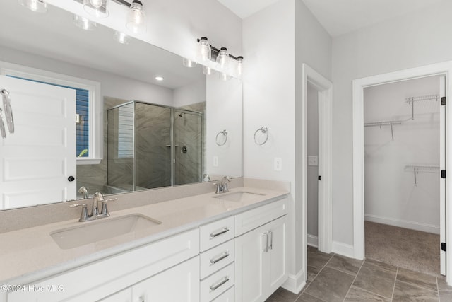 bathroom featuring a shower stall, a spacious closet, double vanity, and baseboards