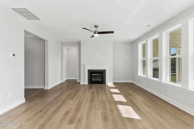 unfurnished living room with ceiling fan, a glass covered fireplace, light wood-type flooring, and baseboards