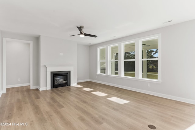 unfurnished living room featuring light wood-style flooring, a glass covered fireplace, baseboards, and ceiling fan