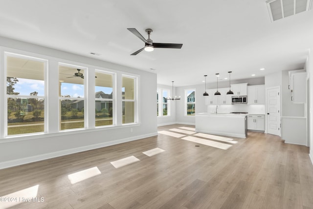 unfurnished living room featuring a chandelier, ceiling fan, light wood-style flooring, baseboards, and recessed lighting