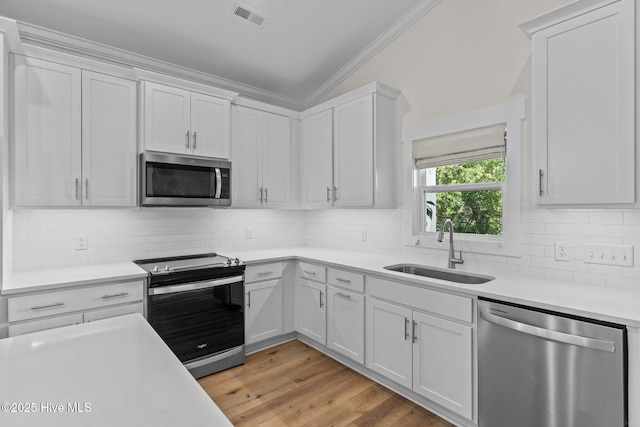 921 Whitecaps Ln, Carolina Beach, NC 28428 - kitchen with stainless steel appliances, ornamental molding, a sink, light countertops, and light wood-style floors