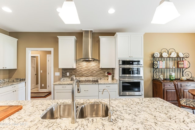 kitchen with wall chimney exhaust hood, a sink, double oven, white cabinets, and recessed lighting