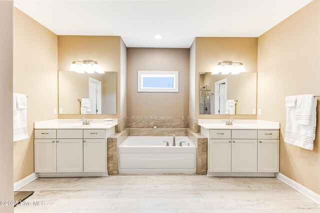 bathroom featuring a garden tub, a shower stall, two vanities, wood finished floors, and recessed lighting