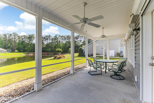sunroom / solarium with a water view, a ceiling fan, outdoor dining area, and view of wooded area