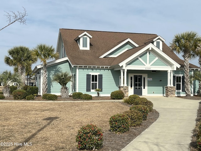 view of front of home with a shingled roof, a porch, and stone siding