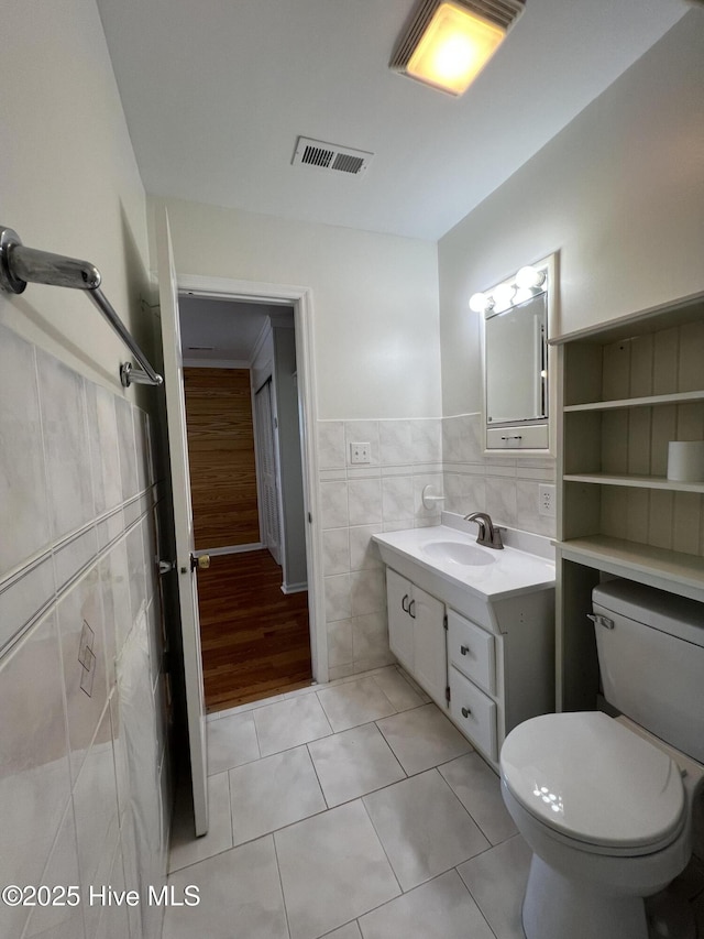 bathroom with tile walls, vanity, tile patterned floors, toilet, and a wainscoted wall
