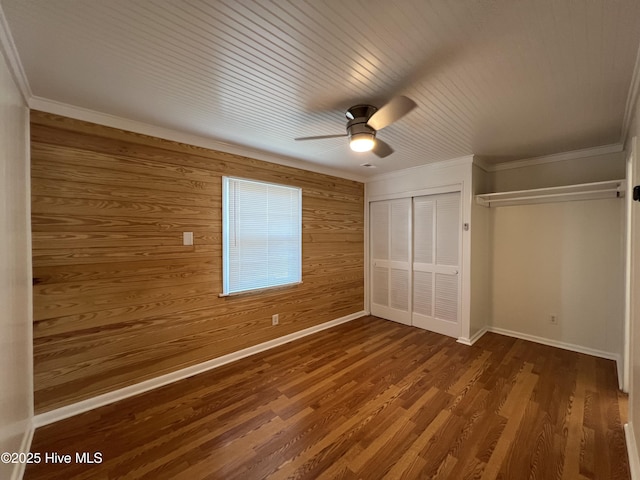 unfurnished bedroom with wooden walls, a closet, wood finished floors, baseboards, and ceiling fan