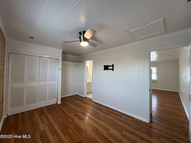 unfurnished bedroom featuring attic access, dark wood-style floors, crown molding, baseboards, and a ceiling fan