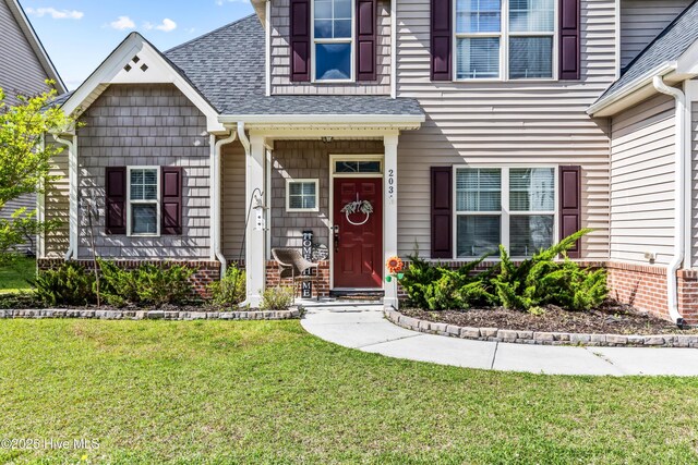 203 Holmes Point Ct, Jacksonville, NC 28546 - property entrance featuring a shingled roof, a lawn, covered porch, and brick siding