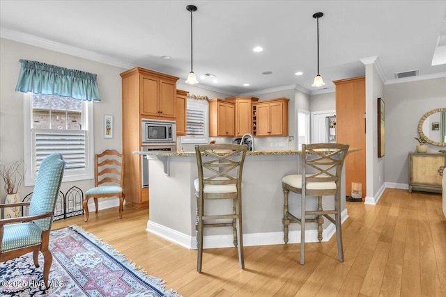 kitchen with stainless steel microwave, oven, light wood-style flooring, ornamental molding, and a breakfast bar