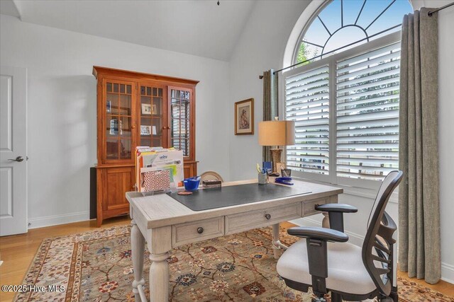 office space with light wood-type flooring, baseboards, and lofted ceiling
