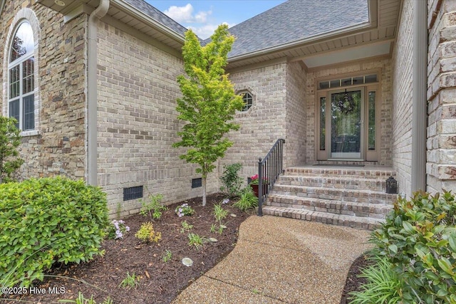 property entrance featuring crawl space, a shingled roof, and brick siding