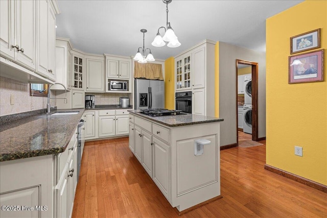 476 Paige Riddick Rd, Gates, NC 27937 - kitchen featuring black appliances, a sink, a chandelier, stacked washer and clothes dryer, and decorative backsplash