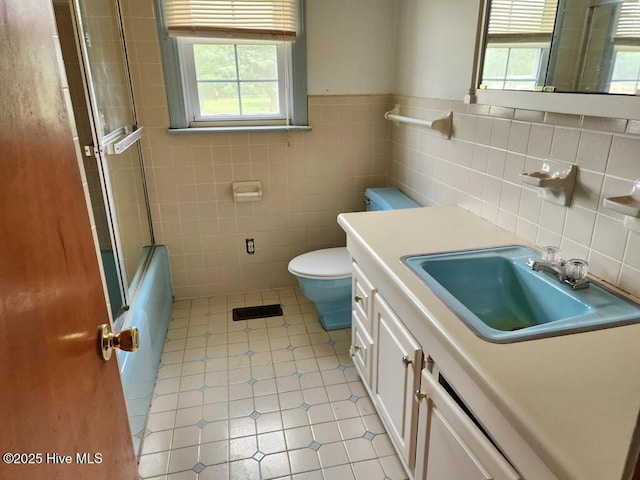 bathroom featuring tile walls, tile patterned flooring, toilet, vanity, and wainscoting