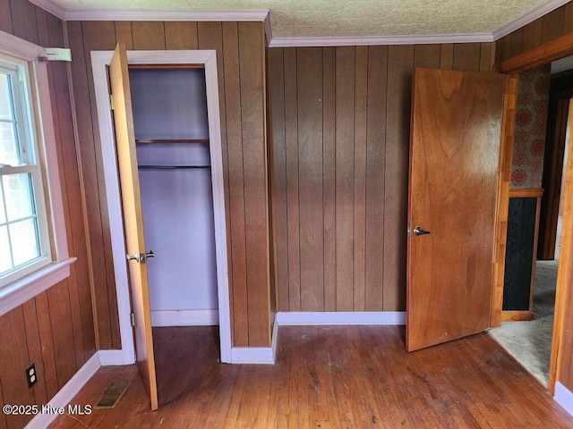 unfurnished bedroom with wood-type flooring, baseboards, ornamental molding, and wood walls