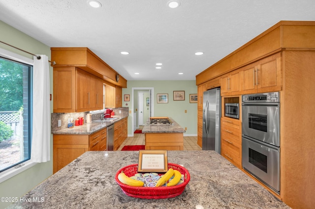 kitchen featuring stainless steel appliances, a kitchen island, recessed lighting, light stone countertops, and brown cabinets