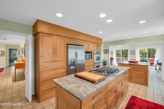 kitchen featuring stainless steel appliances, a center island, light tile patterned floors, light stone counters, and recessed lighting