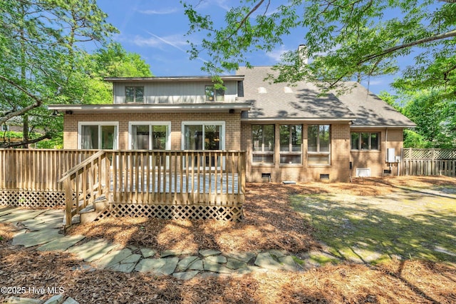 back of property with brick siding, a wooden deck, fence, and roof with shingles