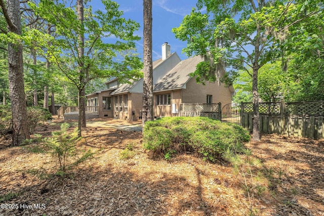 back of house featuring a chimney, fence, brick siding, and a gate