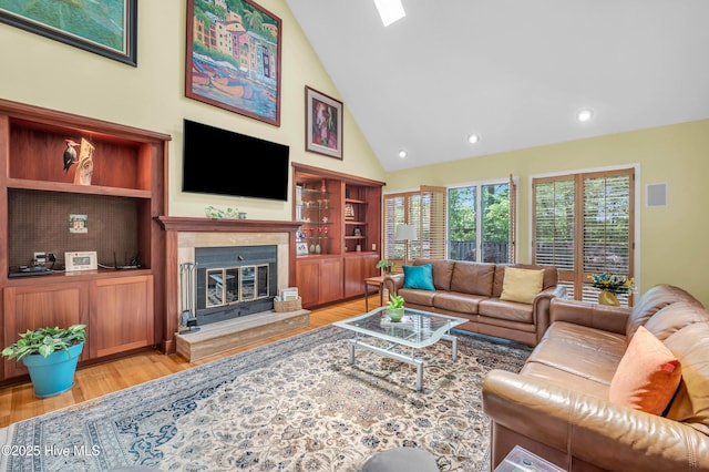 living room with light wood finished floors, high vaulted ceiling, a glass covered fireplace, recessed lighting, and built in features