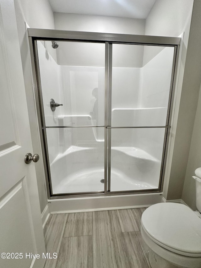 bathroom with toilet, a stall shower, and wood finished floors