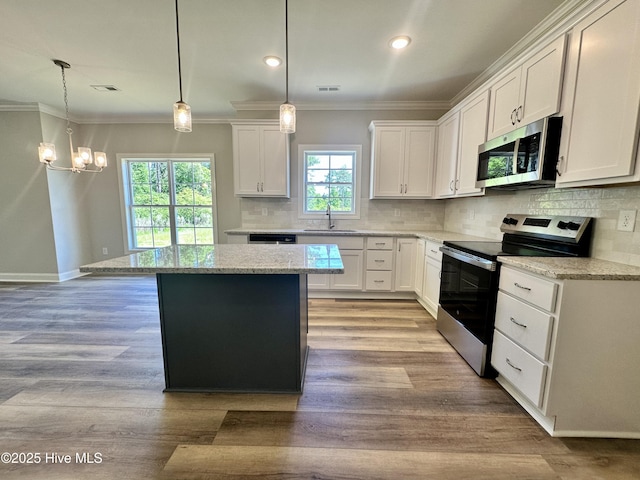 kitchen with appliances with stainless steel finishes, a sink, ornamental molding, a kitchen island, and white cabinetry