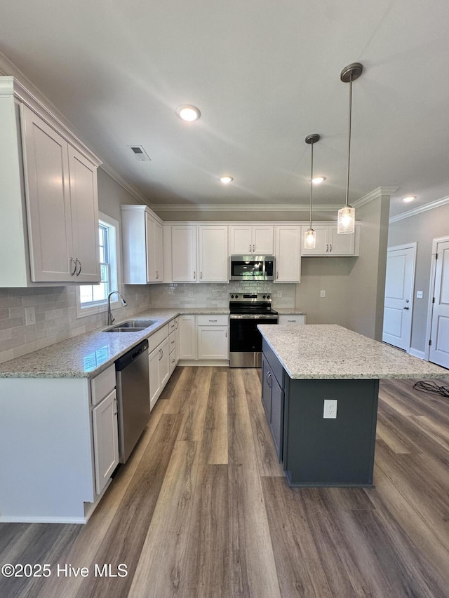 kitchen with appliances with stainless steel finishes, a sink, ornamental molding, dark wood-style floors, and white cabinetry