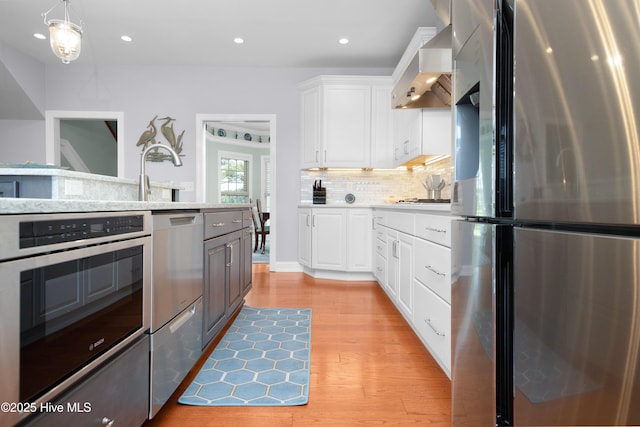 555 Dawson Creek Dr, Arapahoe, NC 28510 - kitchen featuring stainless steel appliances, wall chimney range hood, light wood-style flooring, white cabinetry, and backsplash