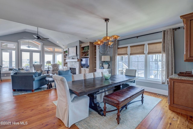 dining room featuring a chandelier, a ceiling fan, vaulted ceiling, light wood finished floors, and a fireplace