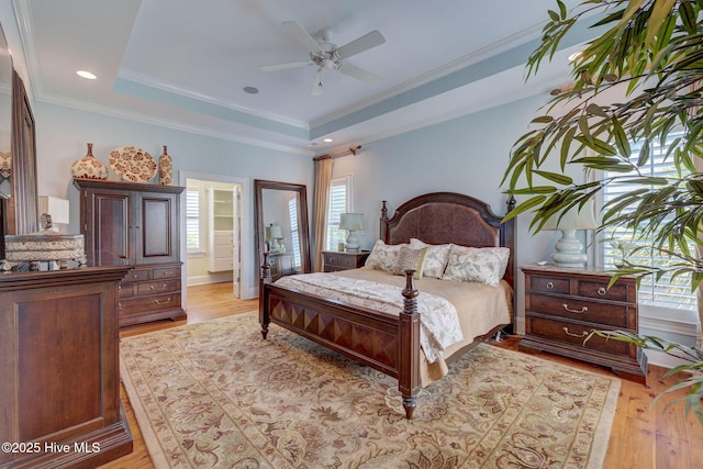 bedroom with light wood-type flooring, a tray ceiling, ornamental molding, baseboards, and a ceiling fan