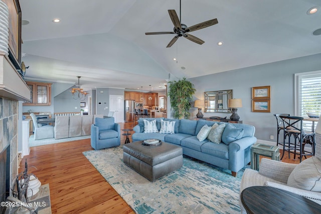 living room featuring a fireplace, vaulted ceiling, ceiling fan, a chandelier, and light wood-style flooring