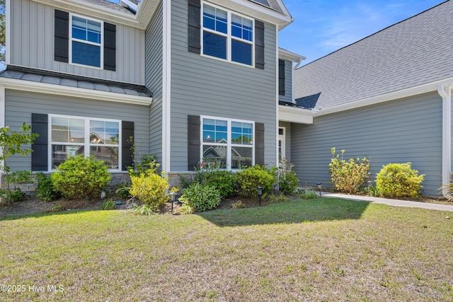rear view of house featuring a lawn, board and batten siding, a shingled roof, and a standing seam roof