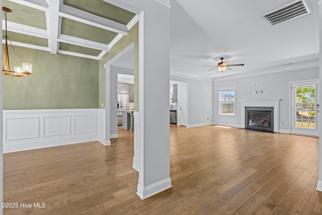 unfurnished living room featuring plenty of natural light, a ceiling fan, crown molding, a fireplace with flush hearth, and wood finished floors