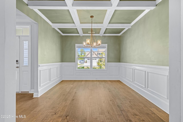 unfurnished dining area with a chandelier, hardwood / wood-style floors, beamed ceiling, coffered ceiling, and a wainscoted wall