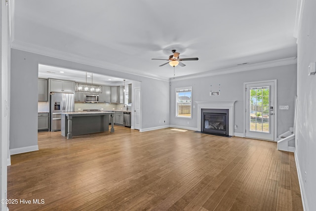 unfurnished living room featuring ceiling fan, plenty of natural light, a fireplace with flush hearth, wood finished floors, and crown molding