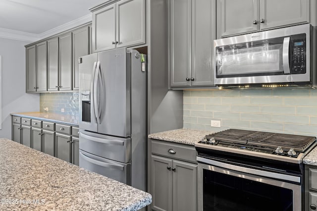 kitchen with stainless steel appliances, gray cabinetry, backsplash, crown molding, and light stone counters
