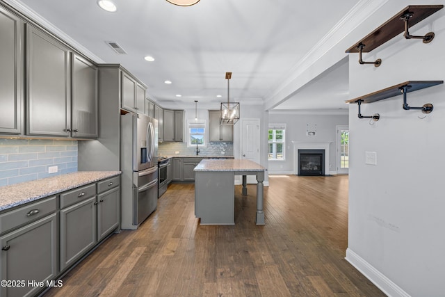 kitchen with gray cabinets, appliances with stainless steel finishes, crown molding, open floor plan, and backsplash