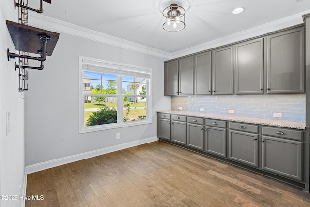 kitchen with gray cabinetry, baseboards, ornamental molding, decorative backsplash, and wood finished floors