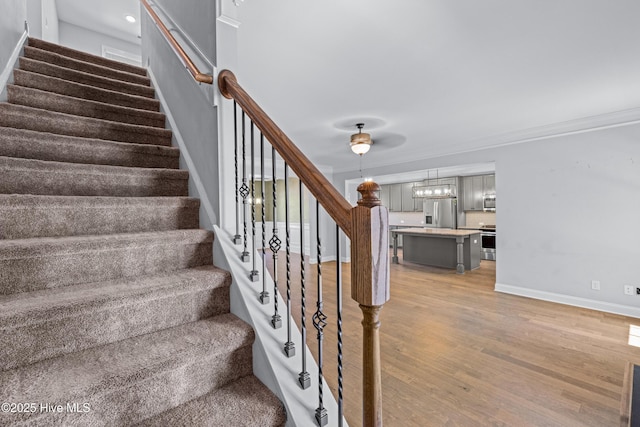 stairs with wood finished floors, baseboards, and ornamental molding
