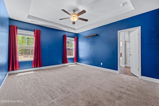 empty room featuring a raised ceiling, ceiling fan, carpet flooring, and baseboards