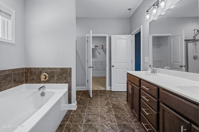 bathroom featuring a walk in closet, a bath, double vanity, and baseboards