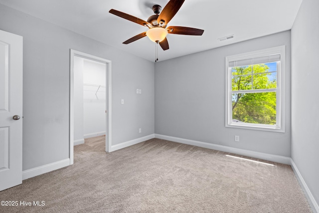 unfurnished bedroom featuring carpet flooring, a walk in closet, baseboards, a closet, and ceiling fan