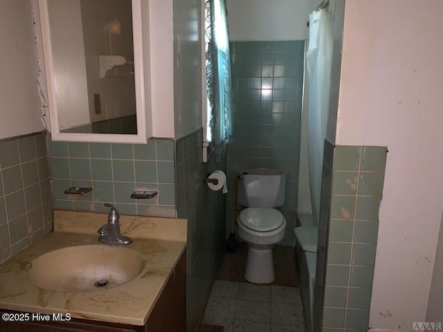full bathroom featuring tile walls, toilet, vanity, and a wainscoted wall