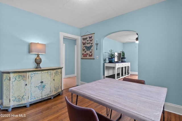 dining area featuring arched walkways, wood finished floors, baseboards, and a ceiling fan